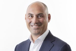 smiling professional headshot of a bald man in a navy suit and white shirt.",